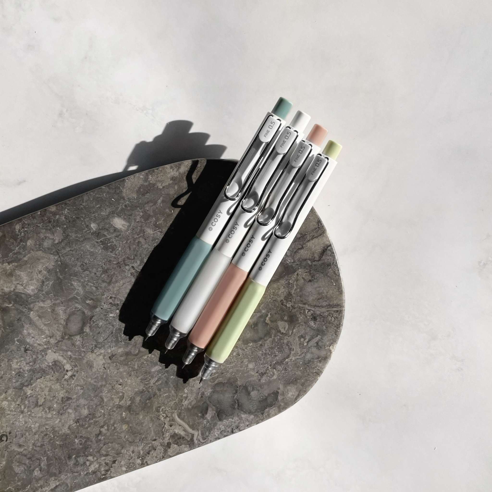 Gelstifte-Set «Cosy» 0,5mm in Pastellfarben mit rutschfester Griffzone und schwarzer Tinte auf grauem Stein unter natürlichem Licht